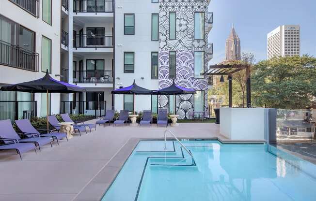 a swimming pool with chairs and umbrellas in front of an apartment building