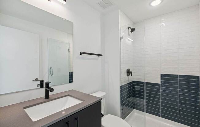 A modern bathroom with a sink, mirror, toilet, and shower.