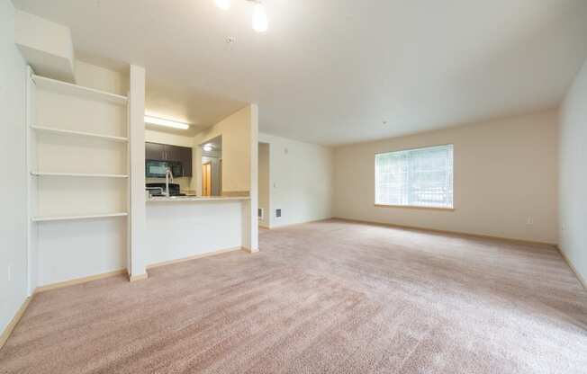 an empty living room with a kitchen in the background