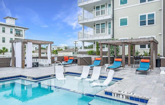 a swimming pool with chairs and a building in the background
