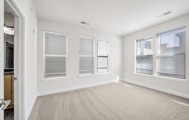 A room with a carpeted floor and three windows.