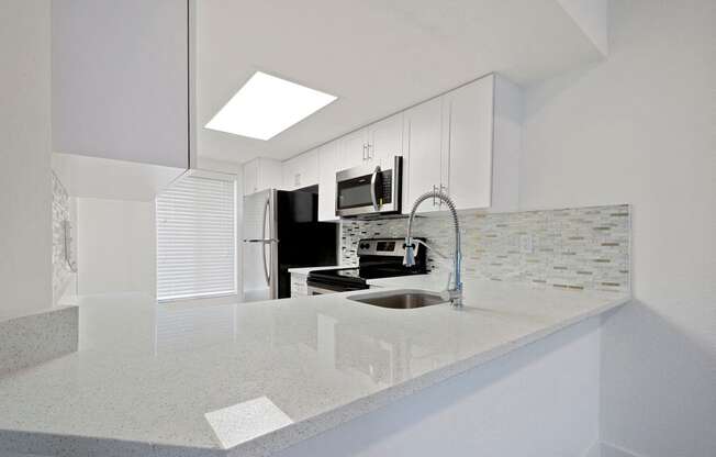 Kitchen with long counter top, tiled back-splash and stainless steel refrigerator, microwave, and oven