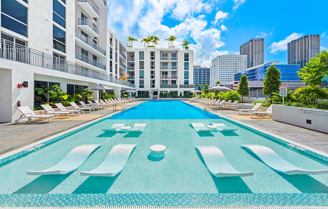 a large pool with lounge chairs and umbrellas in front of a building