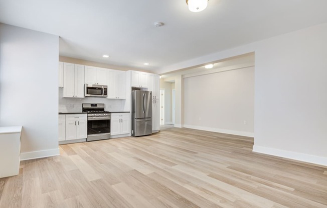 a renovated living room and kitchen with white walls and wood flooring