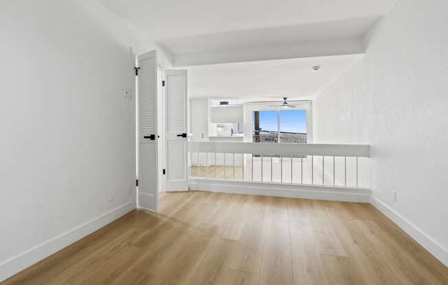 the living room and balcony of an apartment with wood floors and white walls