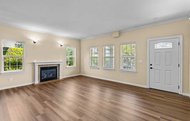 Little Tuscany Apartments & Townhomes - Living Room showing fireplace, multiple windows and front door. Vinyl plank wood flooring, white woodwork