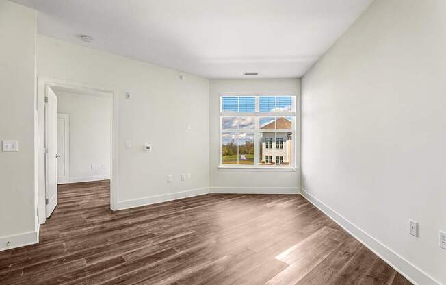 A room with wooden flooring and a window showing a house.