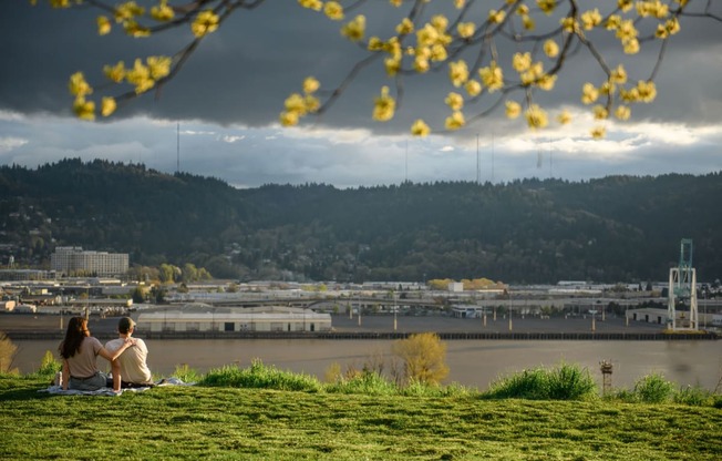 a couple sitting on a hill overlooking a river and a city