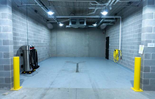 A large, empty room with a concrete floor and walls, equipped with a bike rack and a trash can.
