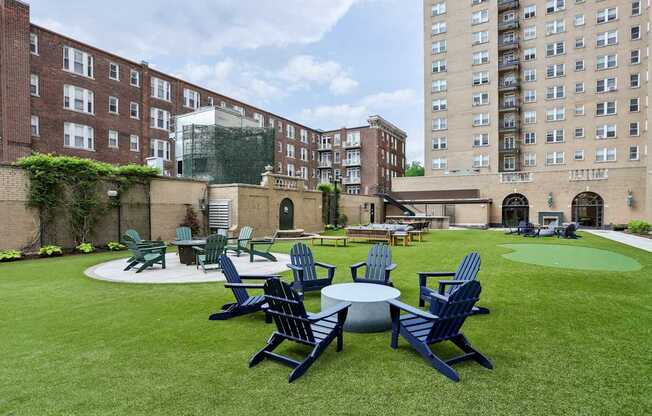 A lawn with chairs and tables is surrounded by buildings.