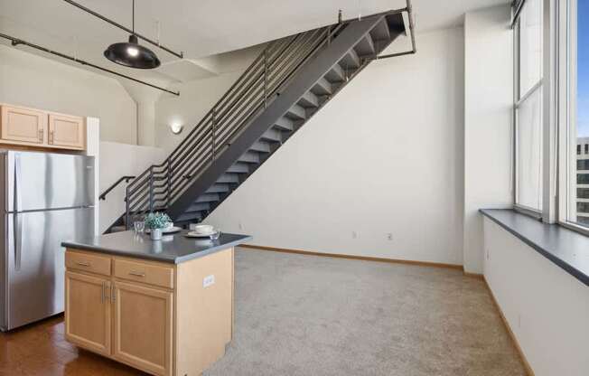 a living room with white walls and a kitchen with a counter and stairs