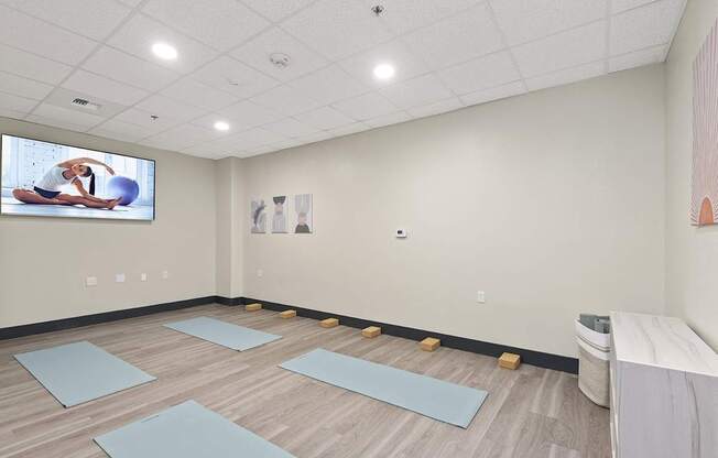 A yoga studio with mats on the floor and a TV screen showing a yoga class.