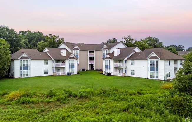 A large white building with multiple windows and balconies is surrounded by greenery.