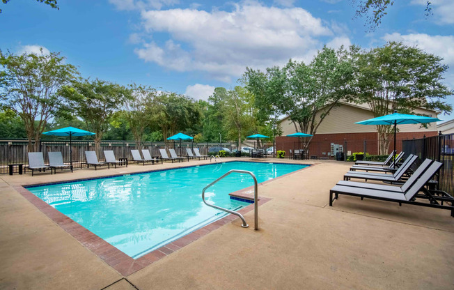 our resort style swimming pool is surrounded by lounge chairs and umbrellas