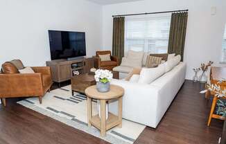 A living room with a white couch, a brown leather chair, a wooden coffee table, and a flat-screen TV.