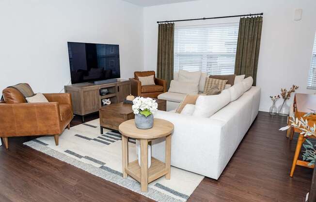 A living room with a white couch, a brown leather chair, a wooden coffee table, and a flat-screen TV.