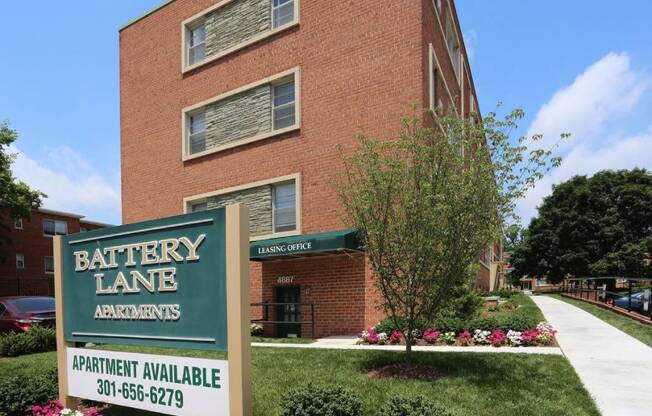 A sign for Battery Lane Apartments is in front of a brick building.