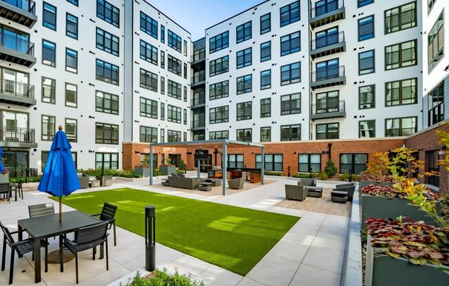 an outdoor courtyard with a lawn and tables in front of an apartment building