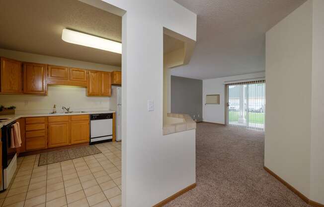 A kitchen with a living room in the background. Pinehurst Apartments | 2 Bedroom