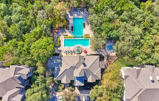An aerial view of a house with a pool surrounded by trees.