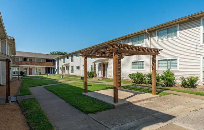 a pathway between two apartment buildings with a wooden pergola