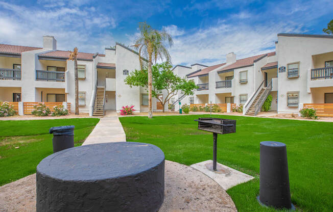 a grassy area with a fire pit and buildings in the background