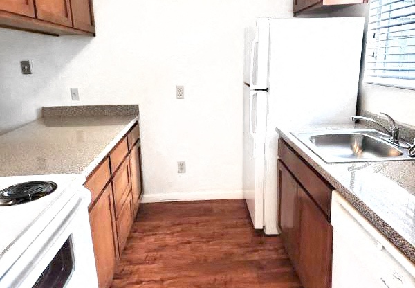 Galley kitchen with wood cabinets, vinyl flooring, oven, refrigerator, sink, and dishwasher