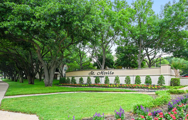 a city with a sign in front of trees and flowers