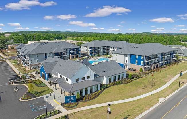 Huntsville, AL Luxury Apartments - The Kelvin - Aerial View of Property Exterior with White and Blue Walls, Grey Roofing, View of Pool, Surrounding Street, and Trees