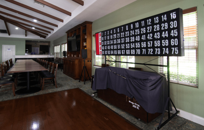 A large room with a long table and chairs, a projector screen, and a wall with numbers from 1 to 75.,A large room with a long table and chairs, a projector screen, and a wall with numbers from 1 to 75.