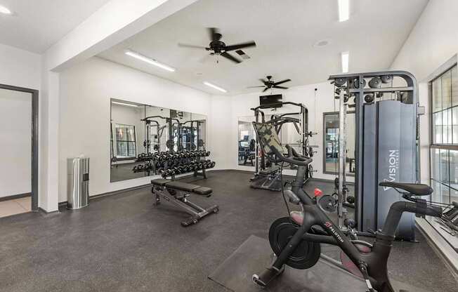 A gym with a variety of equipment including a stationary bike, a treadmill, and a rowing machine.