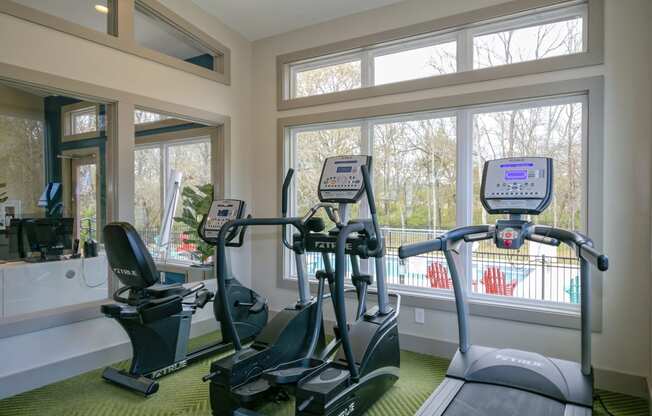 Retreat at Indian Lake Apartments in Hendersonville, TN.. Fitness Center with cardio machines and a large window showing a view of the swimming pool.