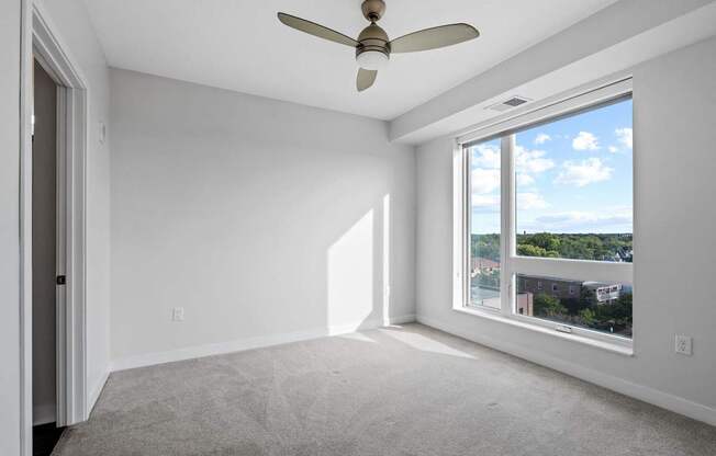 A room with a ceiling fan and a large window overlooking a cityscape.