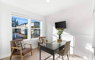 a living room with a desk and chairs and a window