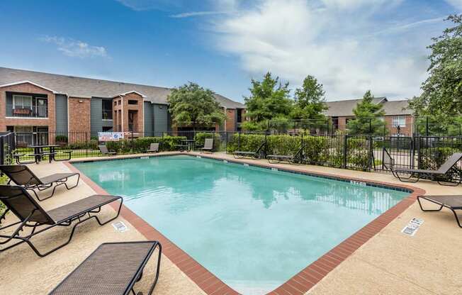 A swimming pool surrounded by lounge chairs and a fence.