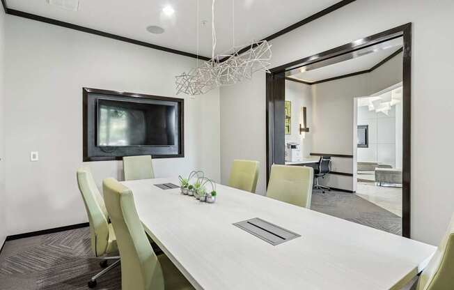 A modern conference room with a long table, chairs, and a television at GreenVue Apartments in Richardson, TX