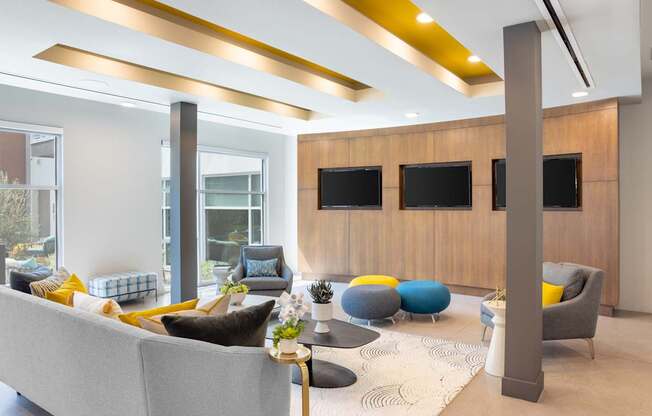 A modern living room with a grey sofa, yellow and blue cushions, a wooden cabinet, and a large window.