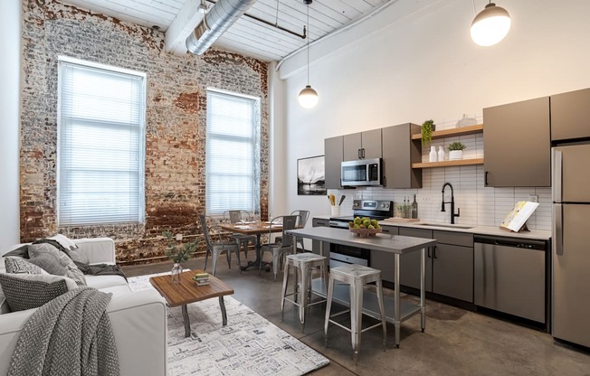 The Mill House floor plan with a kitchen with a white couch and a brick wall at Highland Mill Lofts in Charlotte, North Carolina