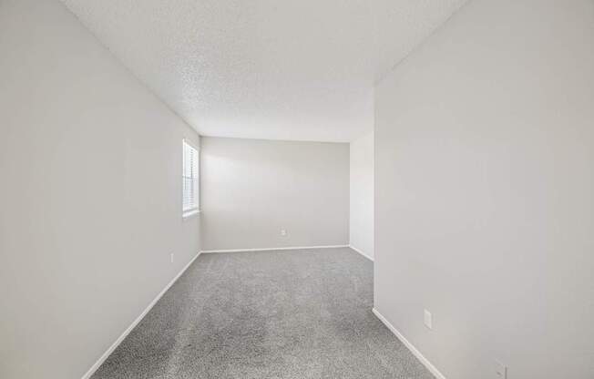 A spacious empty room with carpeted floor and white walls.