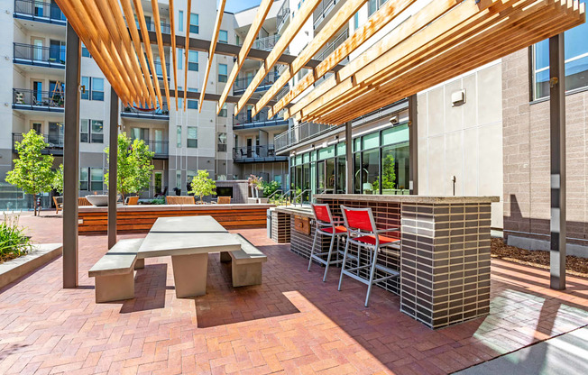 A patio with a table and chairs under a wooden canopy.