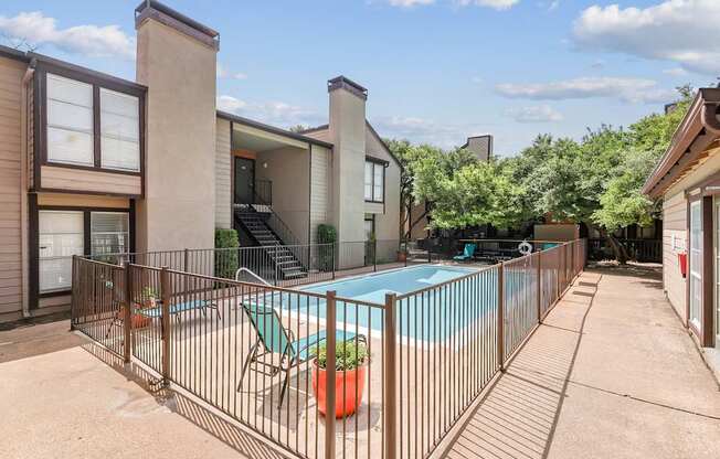 A pool surrounded by a fence with a chair and a potted plant.