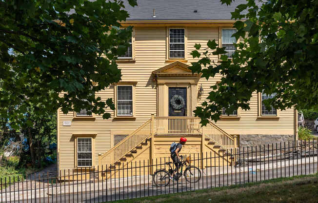 A person riding a bicycle in front of a yellow house.