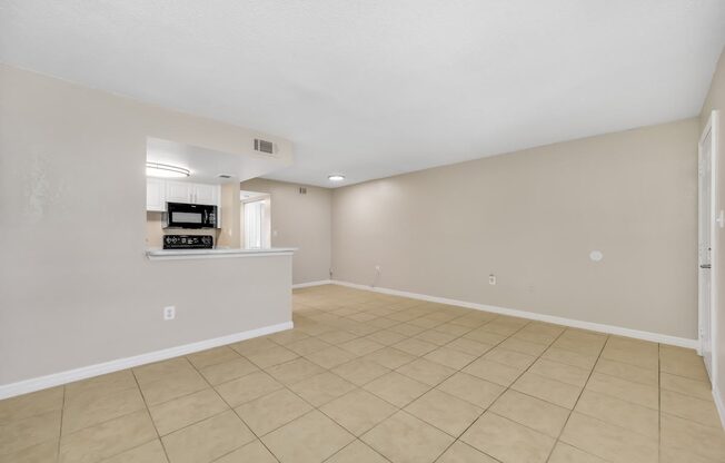 the spacious living room and kitchen of a new home with tiled flooring