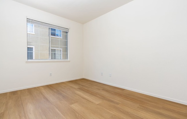 a bedroom with white walls and wood flooring and a window