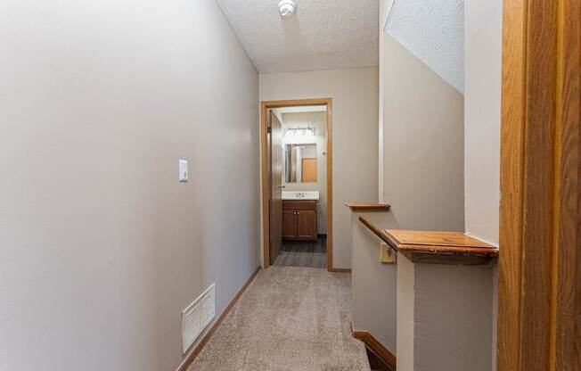 A hallway with a carpeted floor and a wooden railing on the right side.