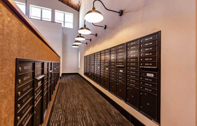 A mailroom here at The Park featuring dark mailboxes, warm wall lighting, and tall windows, creating a modern, organized space with a welcoming and convenient area for residents.
