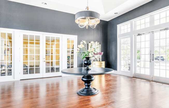 Clubhouse foyer and leasing office with a round black table, dark gray walls, wood flooring, chandelier, and large windows and doors