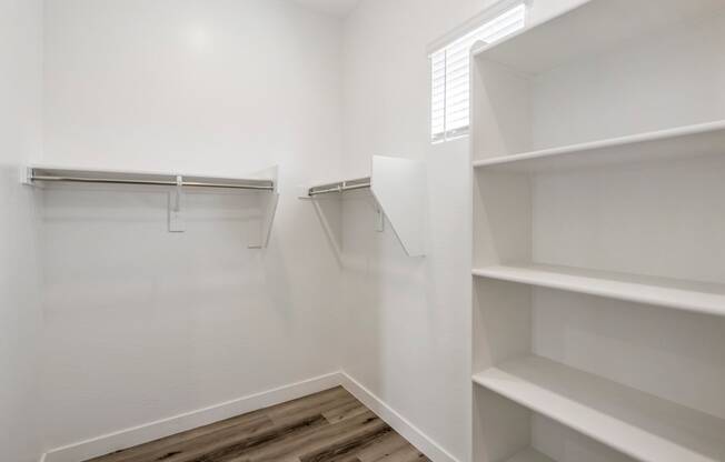 a spacious walk in closet with white walls and wood flooring