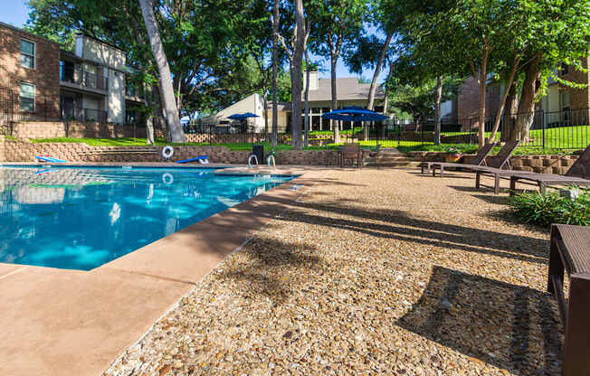 A swimming pool surrounded by a gravel area and trees.