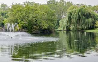 a fountain in the middle of a lake with trees in the background at Evergreen Luxury Apartments, Merrillville